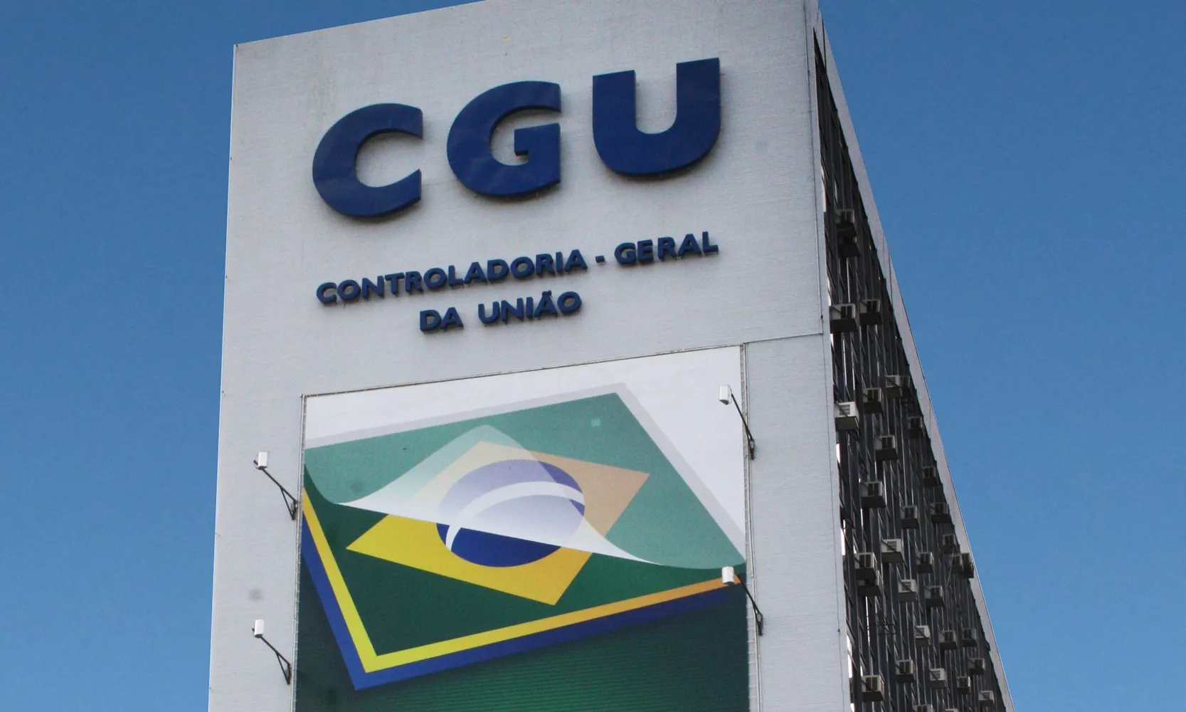Topo do Edifício Darcy Ribeiro, em Brasília, com a sigla CGU e o nome Controladoria-Geral da União em letras azuis sobre a fachada branca.