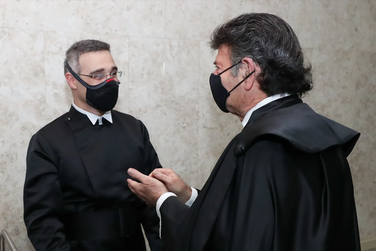 O ministro André Mendonça, de toga e máscara, conversa com outro ministro em um corredor do Supremo Tribunal Federal.