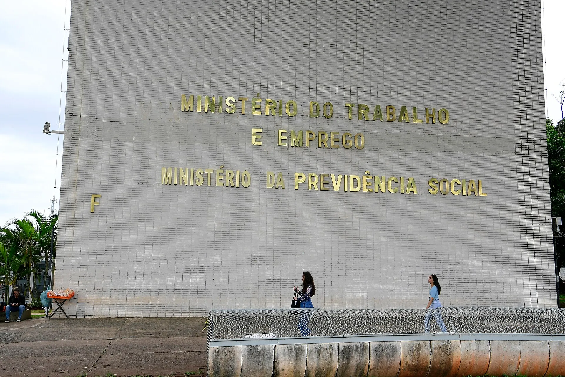 Fachada de azulejos brancos do bloco F da Esplanada dos Ministérios, em Brasília, com os nomes dos ministérios do Trabalho e Emprego e da Previdência Social em letras douradas.