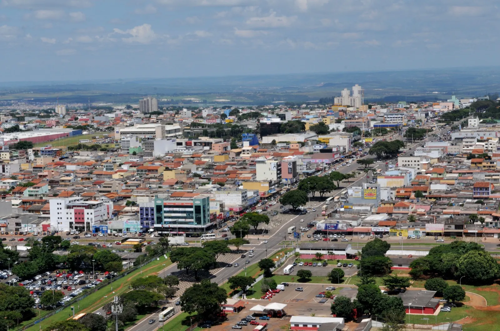 Vista aérea de Ceilândia, no Distrito Federal, com prédios baixos, casas de telhado vermelho, avenidas e uma área arborizada.