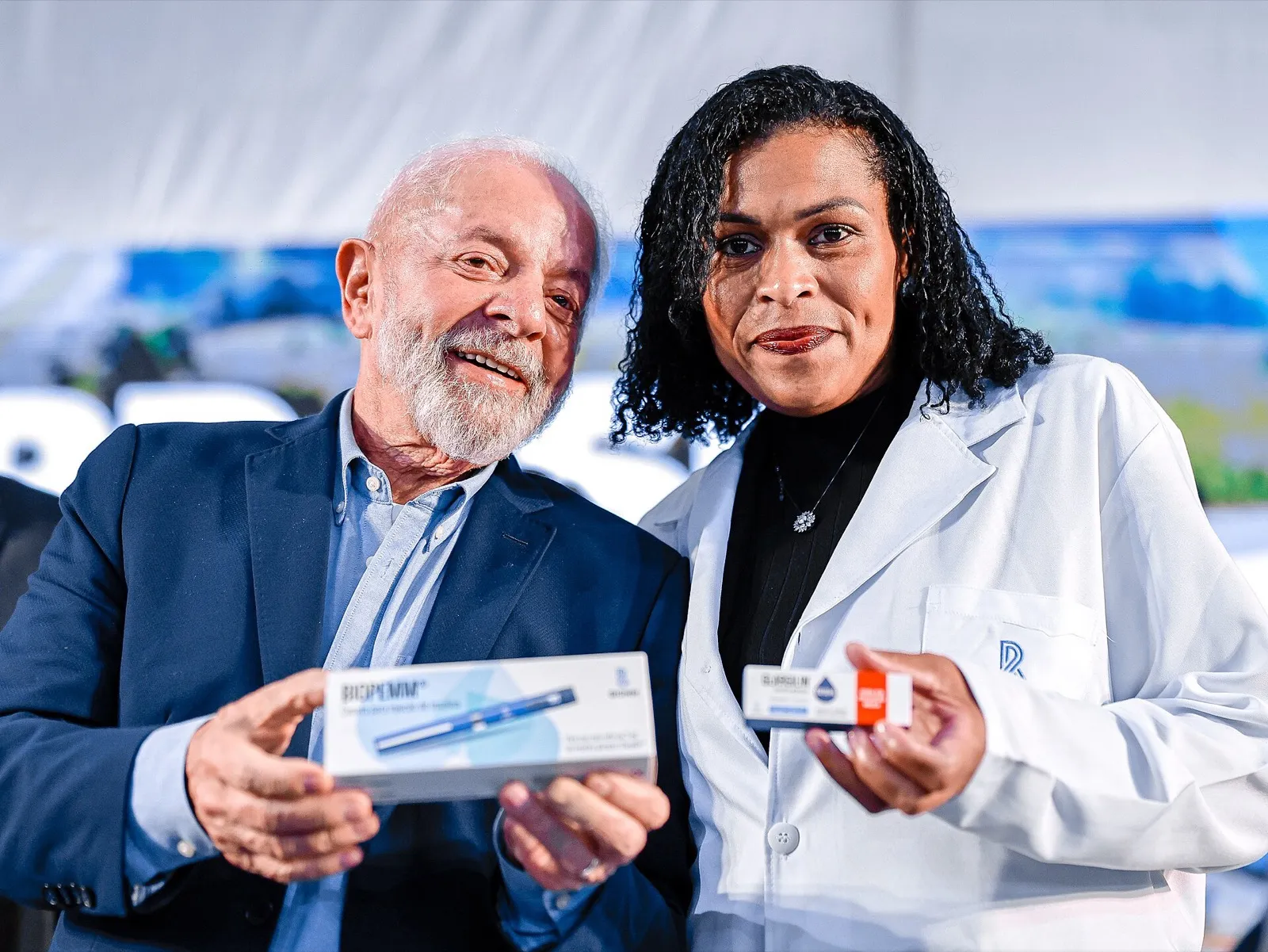 O presidente Lula, de terno azul, e uma mulher de jaleco branco seguram caixas de insulina da Biomm durante cerimônia na fábrica da empresa.